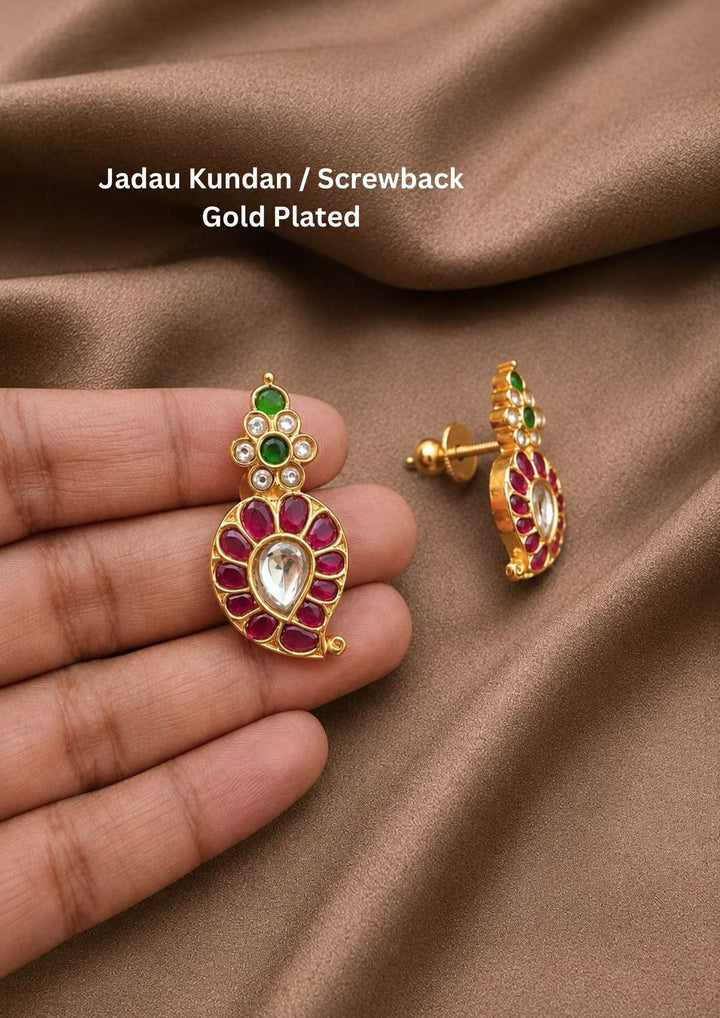 18k gold plated screwback stud earrings featuring a traditional mango or paisley motif inset with a large central teardrop kundan stone surrounded by a pink ruby border, topped with a small accent cluster of green emerald and clear stones. Perfect for weddings, festivals, and daily ethnic wear with premium skin-friendly quality, secure screwback closures, comfortable lightweight fit, and Cash on Delivery available now.