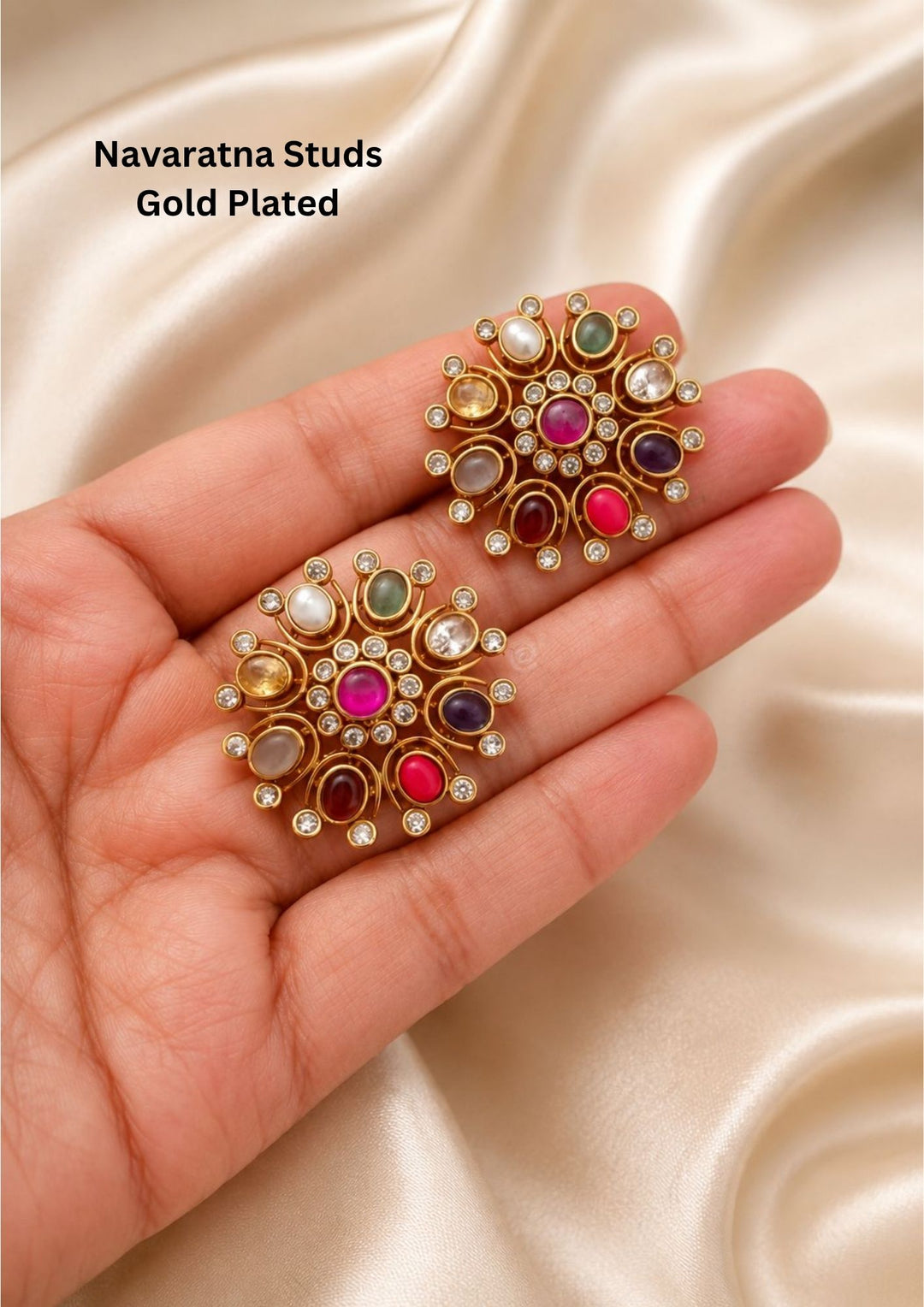 Traditional Navaratna gold plated big stud earrings featuring a classic circular flower design stamped with nine auspicious multi-colored stones. The center features a prominent pink ruby gemstone surrounded by a delicate halo of small white CZ crystals and various colored oval gems—including blue, green, yellow, red, and pearl white—each tipped with a tiny shimmering white stone.