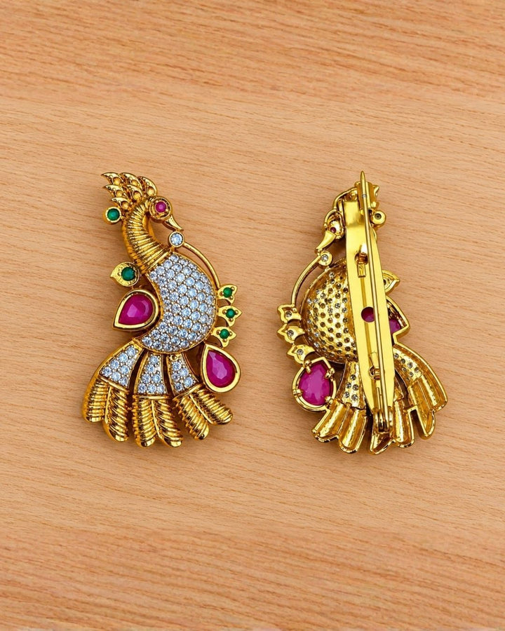 Pair of gold plated peacock saree pins displayed on a light wooden surface, showcasing detailed craftsmanship and decorative stone embellishments.