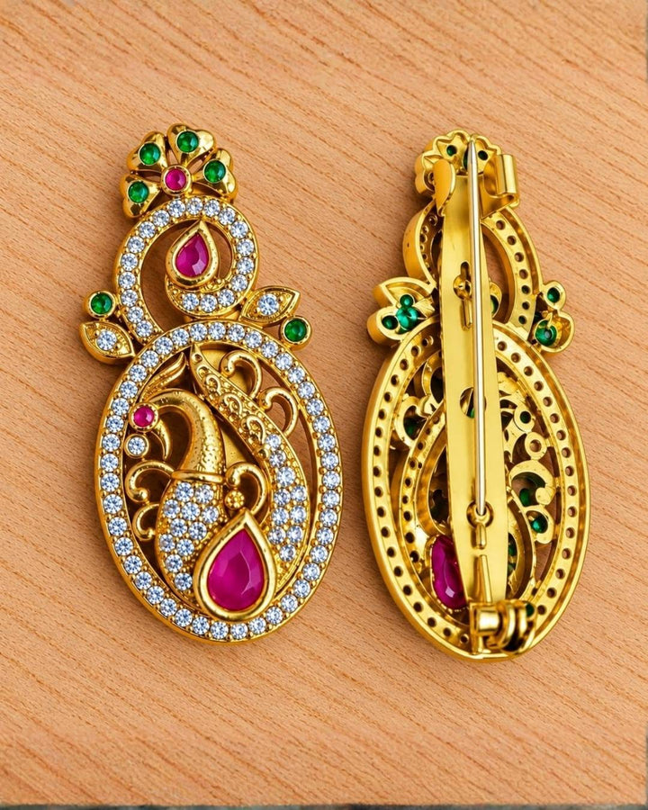 Traditional gold finish peacock brooch with intricate feather detailing, crystal embellishments, and vibrant pink and green stones.