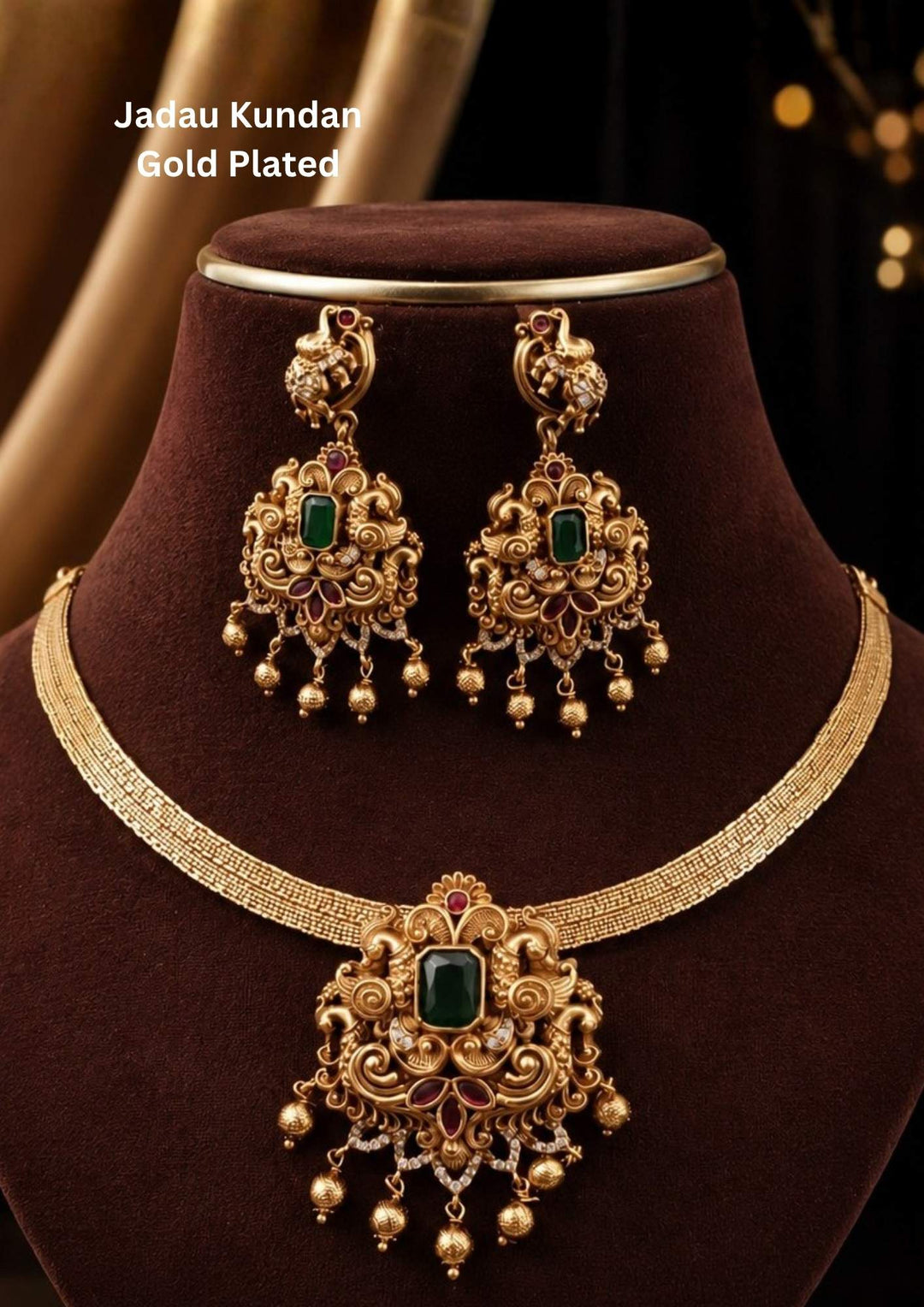 An exquisite antique gold-plated temple jewelry set featuring a flexible, textured mesh collar chain and a grand central pendant. The detailed pendant highlights a large, emerald-cut green stone at the center, surrounded by intricate gold filigree, subtle ruby accents, tiny white crystals, and a row of hanging gold-bead drops. perfect for weddings and festive occasions.