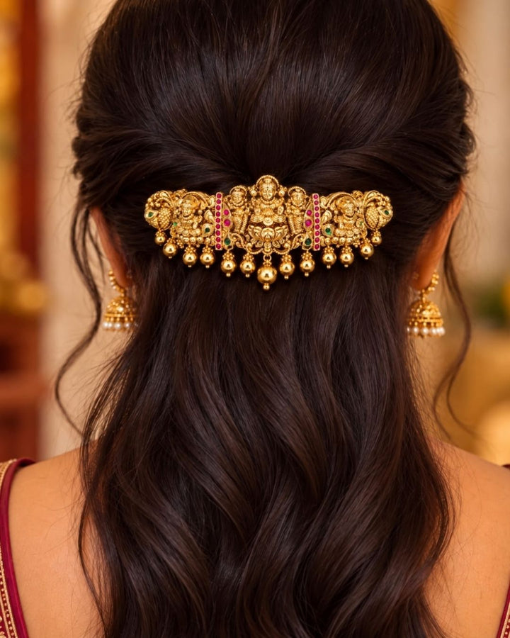 Traditional gold plated designer hair clip featuring multiple Goddess Lakshmi motifs, peacock details, green and ruby-colored stones, intricate floral work, and hanging gold bead embellishments, perfect for festive and traditional hairstyles.