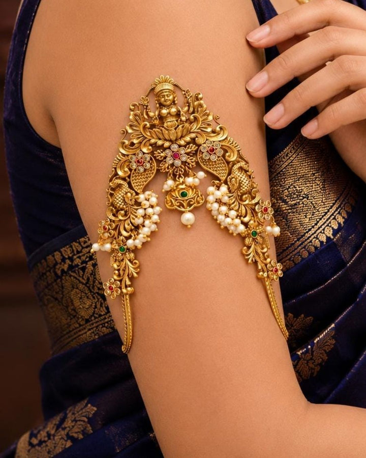 Beautiful Lakshmi Vanki gold plated armlet featuring an ornate Goddess Lakshmi design, peacock-inspired motifs, green and ruby-colored stones, and pearl detailing. Perfect for traditional outfits, festive occasions, temple events, weddings, and gifting.