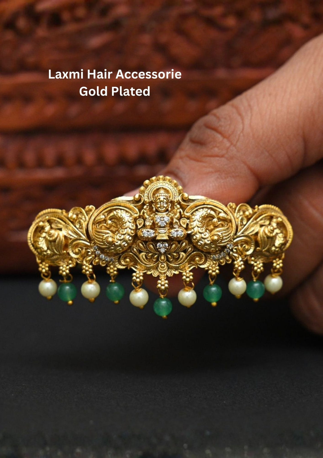 Traditional Laxmi hair accessory gold plated design featuring a beautifully crafted Lakshmi Devi motif at the center surrounded by intricate peacock and floral carvings. The accessory is enhanced with sparkling zircon stone accents, elegant green bead drops and pearl hangings, creating a rich South Indian temple jewelry look perfect for bridal hairstyles, weddings, festivals and classical dance performances.