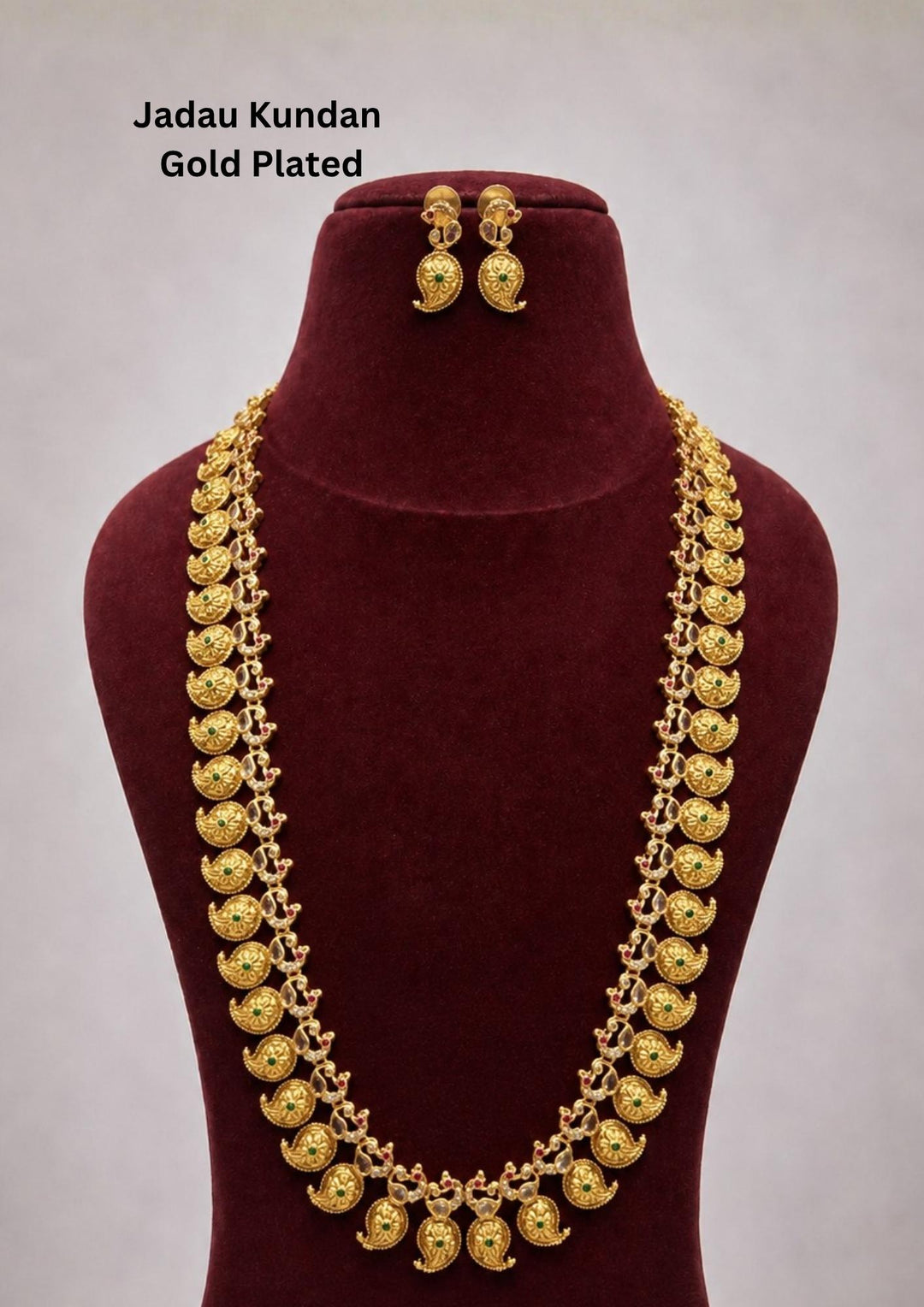 Elegant gold plated long haram featuring intricately crafted paisley motifs adorned with green and ruby stone accents, paired with matching earrings. Inspired by traditional South Indian temple jewellery, this timeless necklace set is perfect for weddings, bridal wear, festivals, and cultural celebrations.