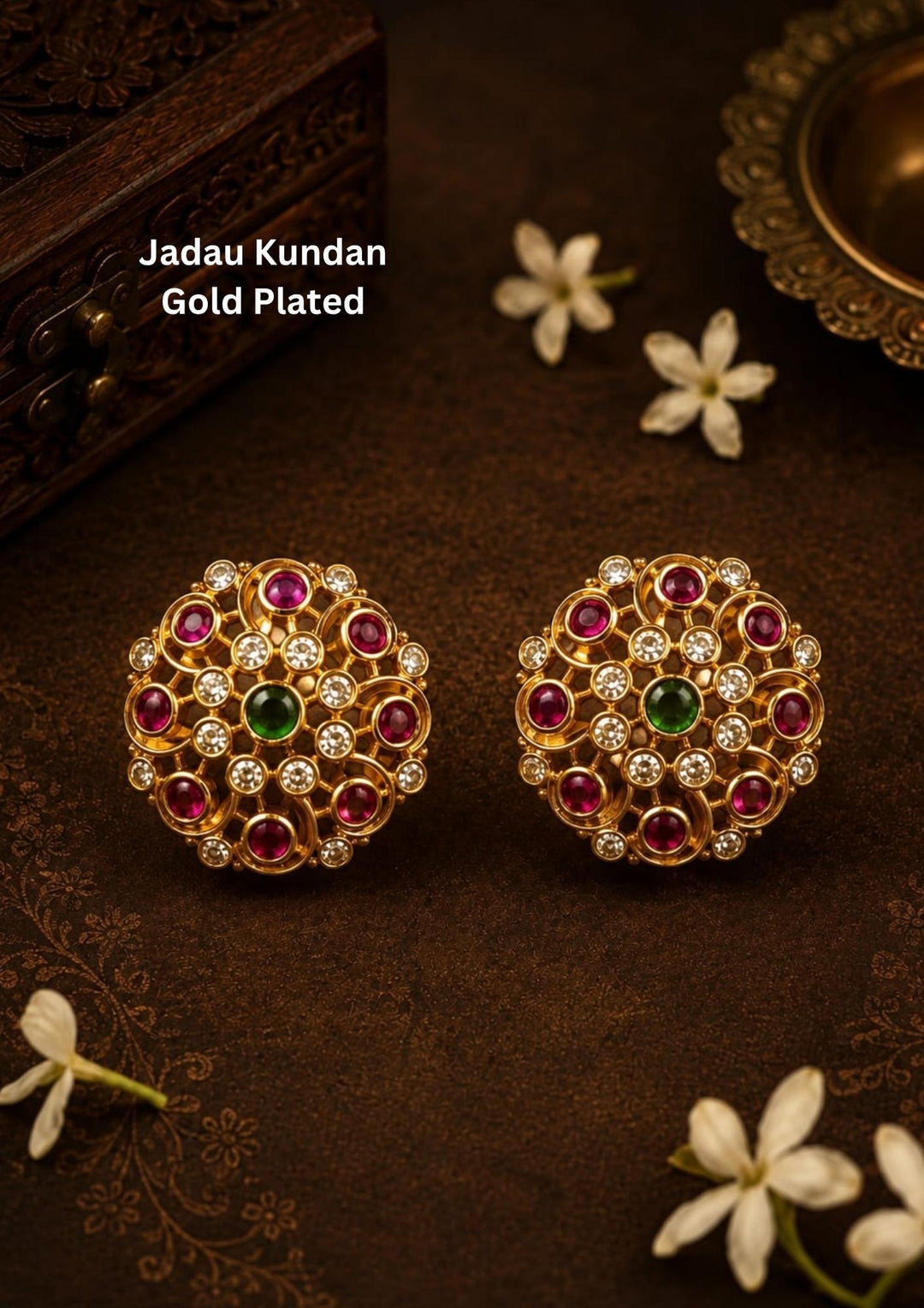 Traditional jadau kundan gold plated stud earrings featuring an intricate circular floral design crafted with radiant ruby-colored stones, sparkling kundan stones and a striking green center stone. The symmetrical pattern and antique-inspired craftsmanship create a rich ethnic appeal suitable for weddings, festivals, poojas and traditional celebrations.