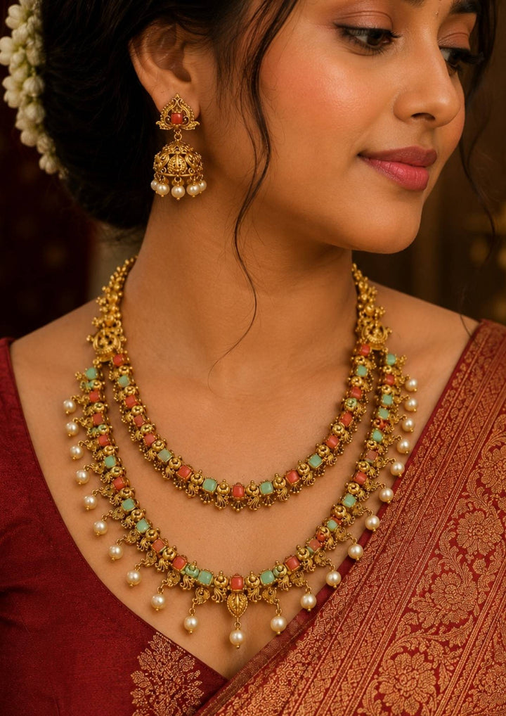 A close-up of a South indian woman wearing Traditional coral gold plated necklace featuring coral stones, pearl drops and intricate handcrafted detailing for an elegant festive appearance jhumka earrings featuring intricate antique detailing with pearl drops Perfect for weddings, festivals and ethnic celebrations.