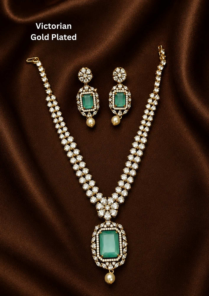Victorian gold plated jewelry set featuring a dual-strand uncut diamond V-shaped chain, a central floral motif, and a prominent rectangular mint green stone pendant finished with an antique oxidized look and a hanging pearl drop. Includes matching hanging earrings. Perfect for receptions, festive events, and sarees with skin-friendly quality, comfortable fitting