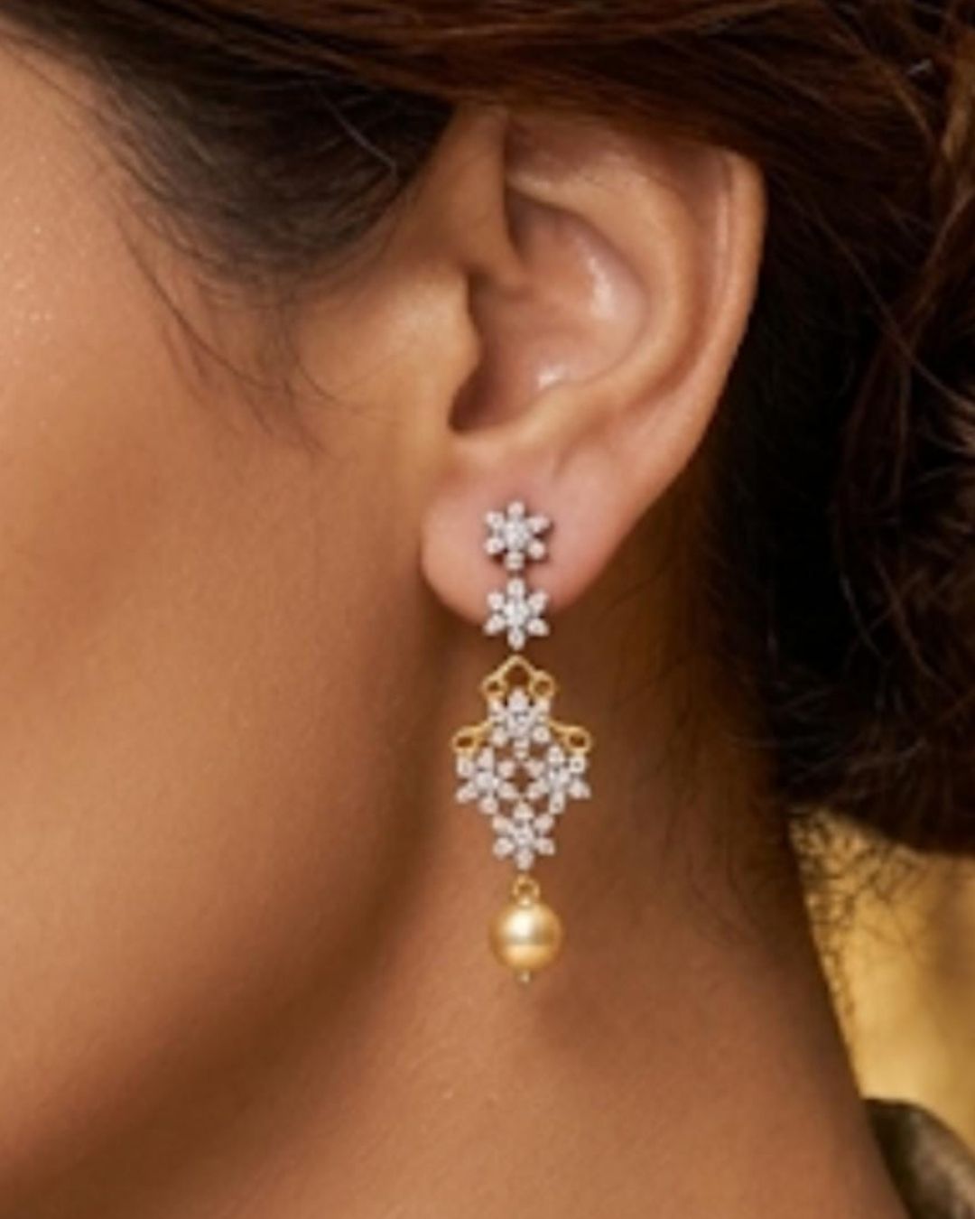 South Indian women Gold plated diamond replica necklace set featuring delicate floral motifs, sparkling stones, and matching drop earrings with pearl accents, displayed on a maroon jewellery bust.