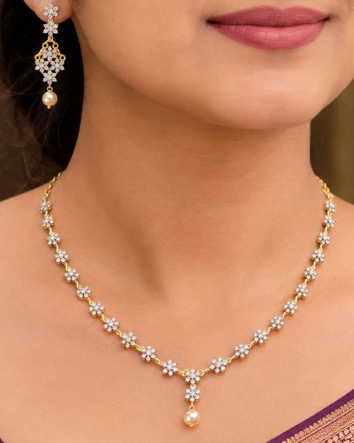 South Indian women Gold plated diamond replica necklace set featuring delicate floral motifs, sparkling stones, and matching drop earrings with pearl accents, displayed on a maroon jewellery bust.