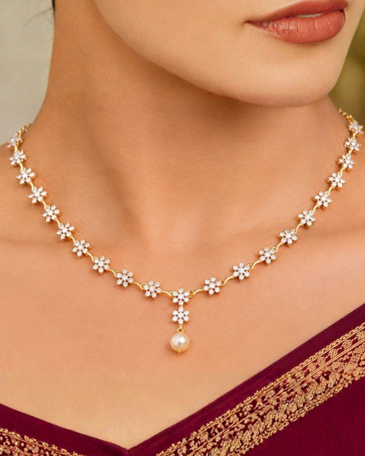 South Indian women Gold plated diamond replica necklace set featuring delicate floral motifs, sparkling stones, and matching drop earrings with pearl accents, displayed on a maroon jewellery bust.