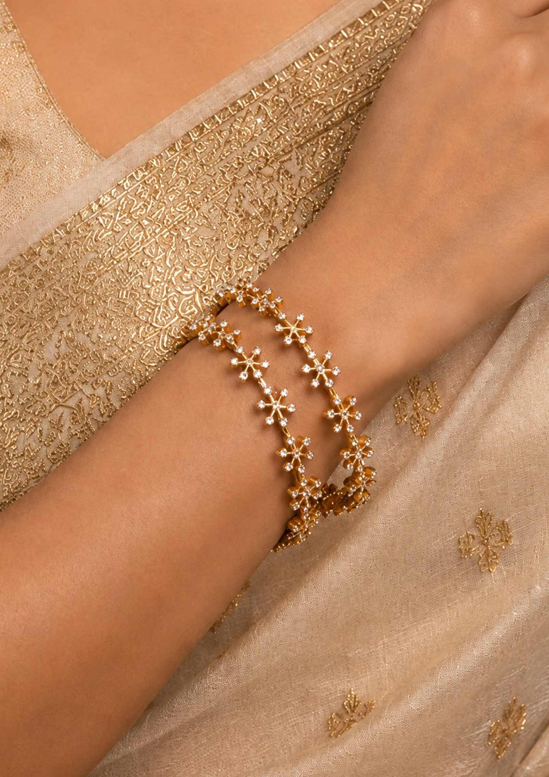 Close-up of a south indian woman wearing Gold Plated Amora Bangles with elegant flower design and sparkling zircon diamond stones placed in a neat pattern all around the bangles. The bangles give a modern and classy jewelry look with shiny gold finish, lightweight comfort, skin-friendly quality, sweat proof finish, anti-fade colour, and are suitable for functions, parties, festivals, office wear, and special occasions.