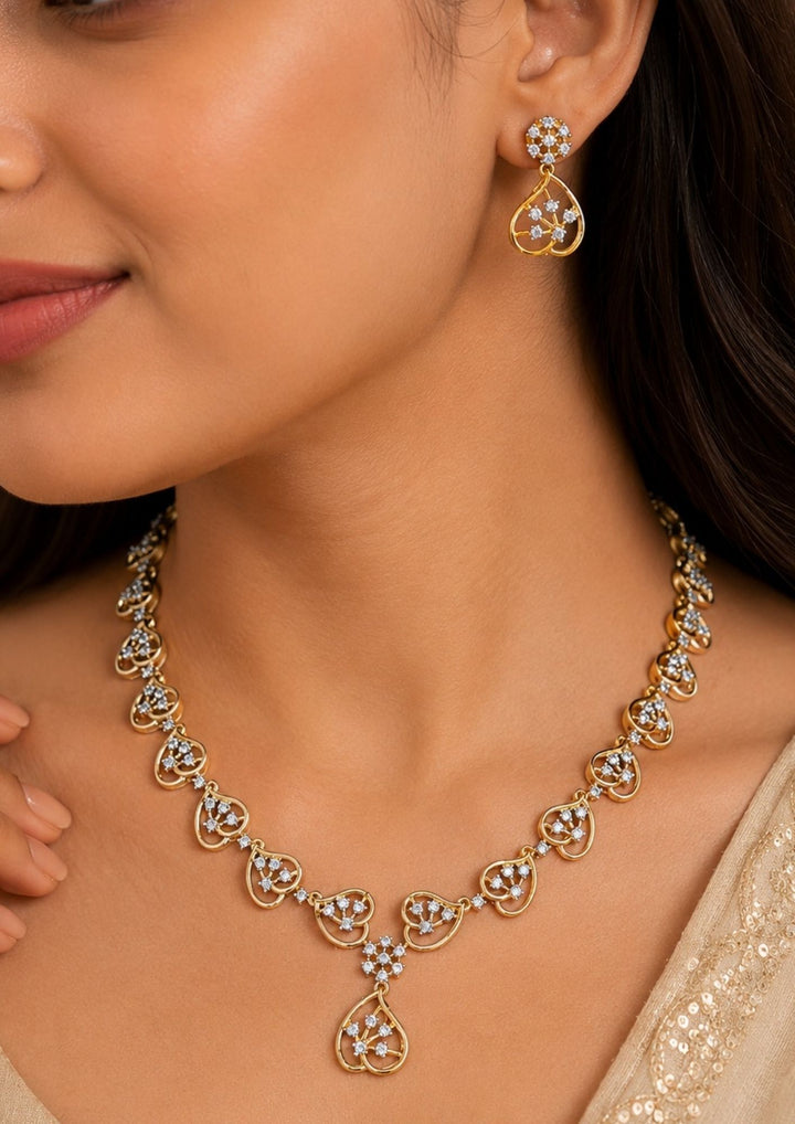 Close-up of a south Indian woman wearing a zircon diamond gold-plated necklace and earring ensemble. The dainty, repeating leafy silhouette design offers a brilliant, radiant sparkle against the rich purple background. This lightweight yet luxurious jewelry set is designed to pair seamlessly with contemporary ethnic wear, evening gowns, or modern bridal reception outfits.