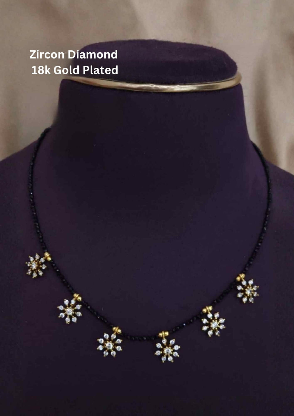 Gold Plated Sankranti Mangalsutra with simple black bead chain design with flower shape and with white stone pattern. The mangalsutra has shiny gold finish, lightweight feel, sweat proof quality, anti-fade colour, skin-friendly finish, and is suitable for daily wear, office wear, festivals, and traditional occasions.