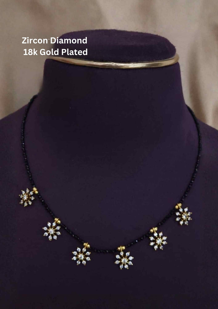 Gold Plated Sankranti Mangalsutra with simple black bead chain design with flower shape and with white stone pattern. The mangalsutra has shiny gold finish, lightweight feel, sweat proof quality, anti-fade colour, skin-friendly finish, and is suitable for daily wear, office wear, festivals, and traditional occasions.