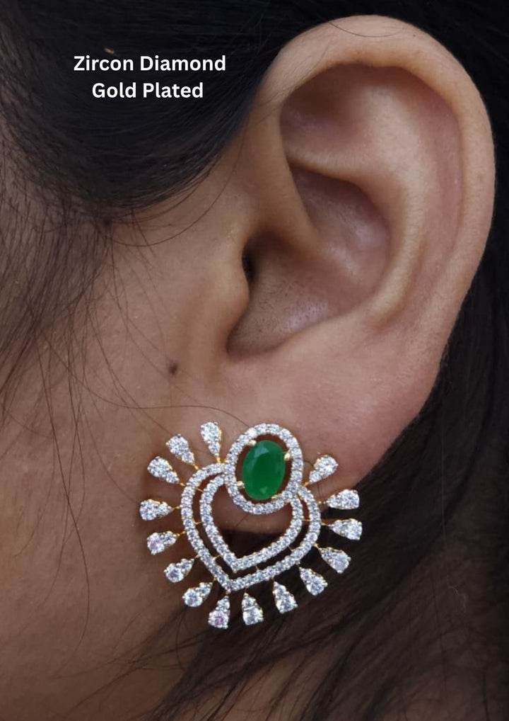 Close-up of an ear wearing a zircon diamond gold-plated earring with a green gemstone.