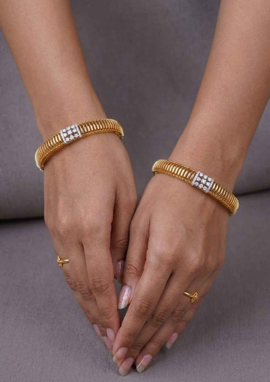 Close-up of a woman's hands elegant Diamond 18K Gold Plated bangles. Designed with a lightweight, three layer design with sparkling white stones, these premium finish bangles are suitable for daily wear, office styling, or festivals.