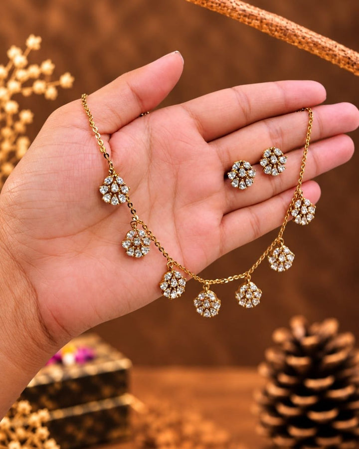 Elegant gold plated necklace with sparkling white zircon stones and floral dangling motifs displayed on a navy blue jewellery bust.