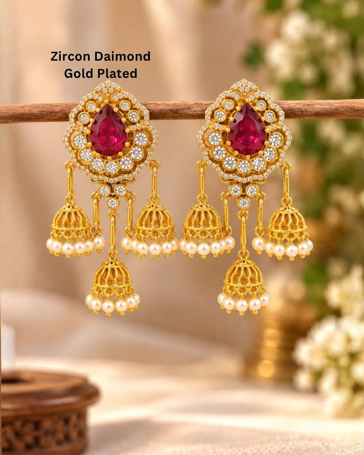 Gold plated zircon diamond jhumka earrings featuring ruby red teardrop stones, clear sparkling stones, and multiple pearl-decorated gold jhumka hangings.