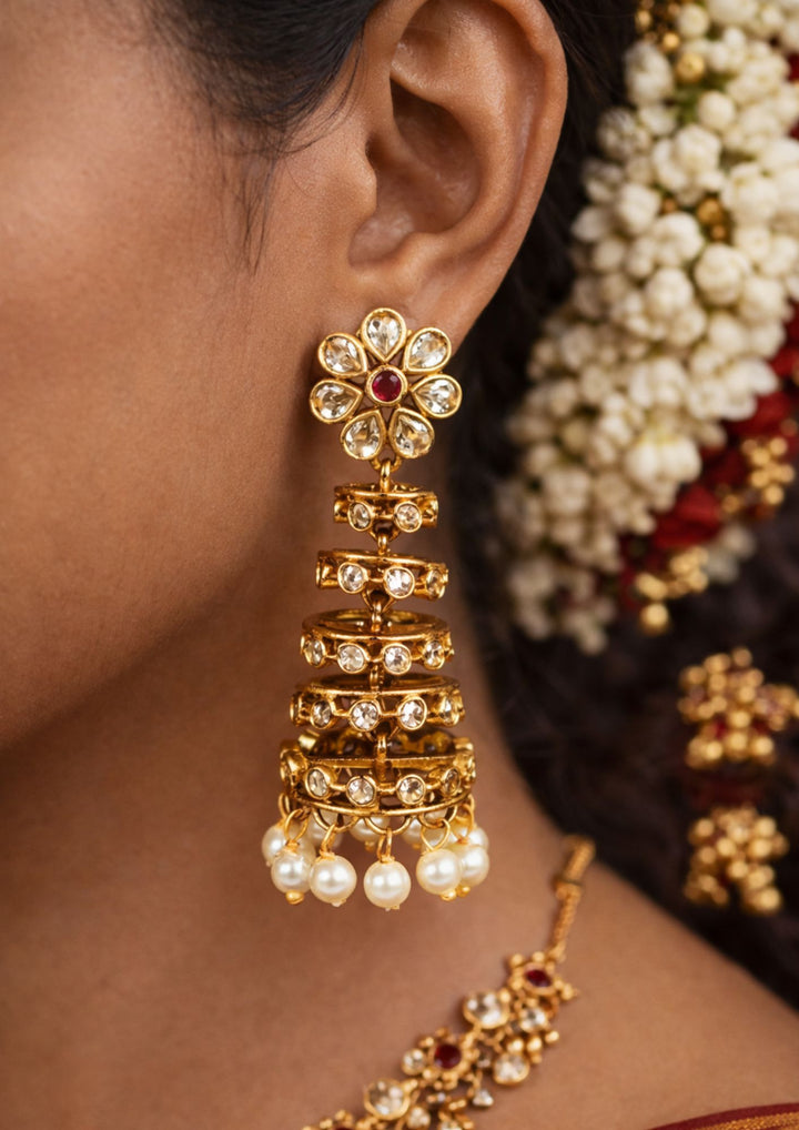 Close-up of a south indian woman wearing Gold Plated Traditional Jhumkas with dome-style buttalu pattern, colorful stone work, and pearl drops that give a grand bridal and festive jewelry look. The earrings come with lightweight comfort, sweat proof finish, anti-fade colour, smooth fitting, and are suitable for weddings, receptions, functions, and celebrations.