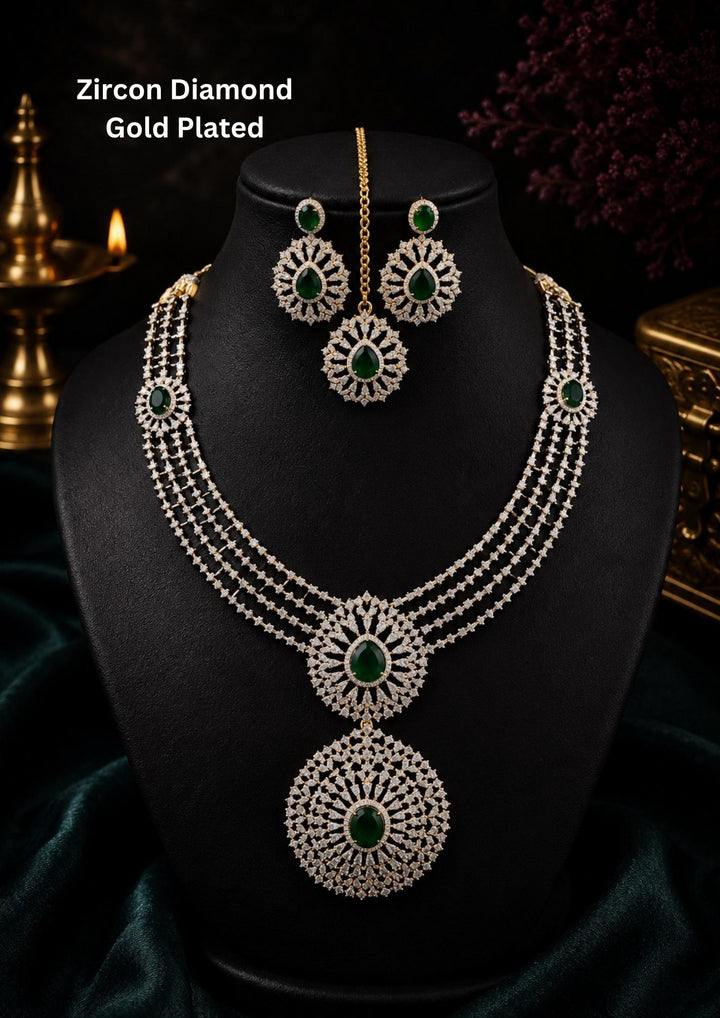 Zircon diamond gold-plated necklace and earrings set designed with 3 row zircon diamonds and in the middle it is designed with green emerald stone and it also has matching earrings designed in the leaf pattern with green emerald stud on the top and it also had magtikka perfect for weddings, bridalwear, festivals and its anti fade color