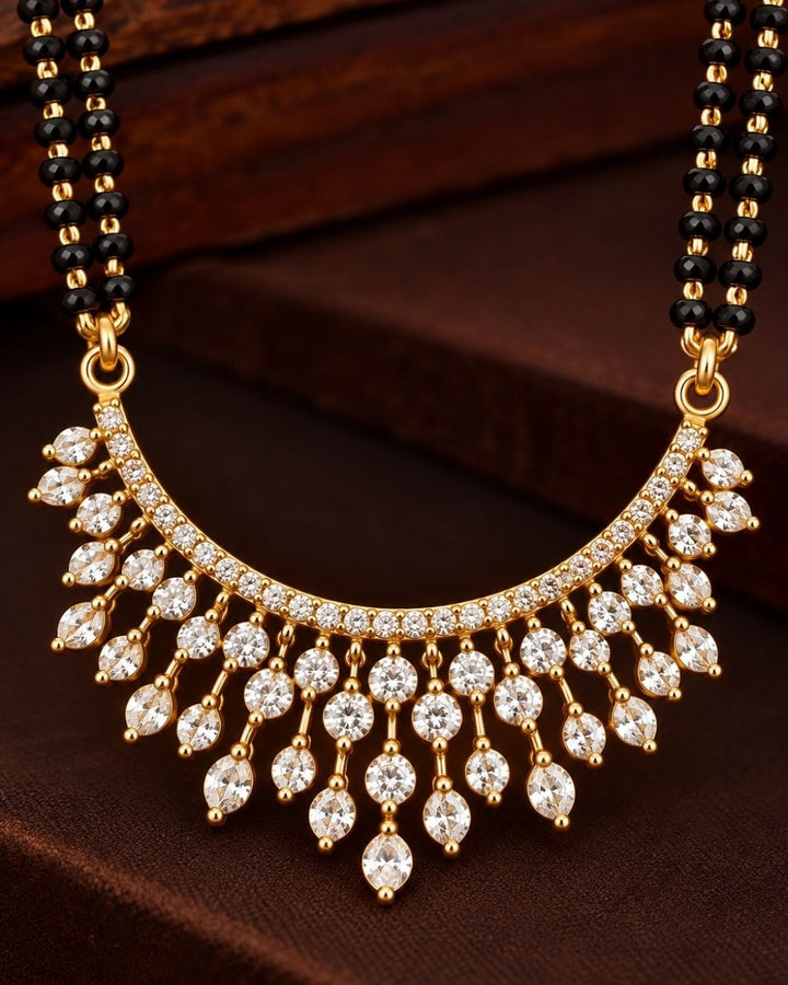 18K Gold Plated Zircon Diamond Mangalsutra set designed with a dual-strand black bead Nallapusalu chain and a half moon-shaped pendant. The pendant show rows of sparkling white zircon stones in a radiating fringe pattern, paired with matching cluster stone stud earrings for a luxurious, premium jewelry finish. Perfect for any ocaasions and dailywaer