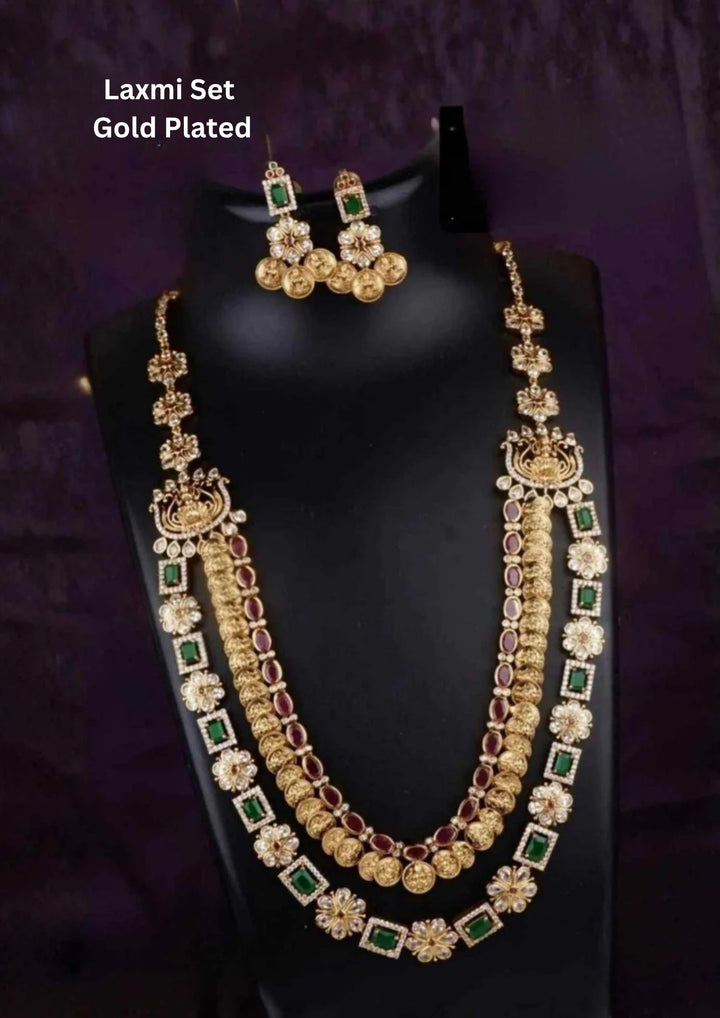 A grand multi-layered gold plated haram set featuring an inner double-strand of embossed Laxmidevi coin links (Kasu Mala) trimmed with rubies. The outer third layer consists of geometric square frames inlaid with emerald green stones and kundan crystals, complete with matching coin drop earrings.