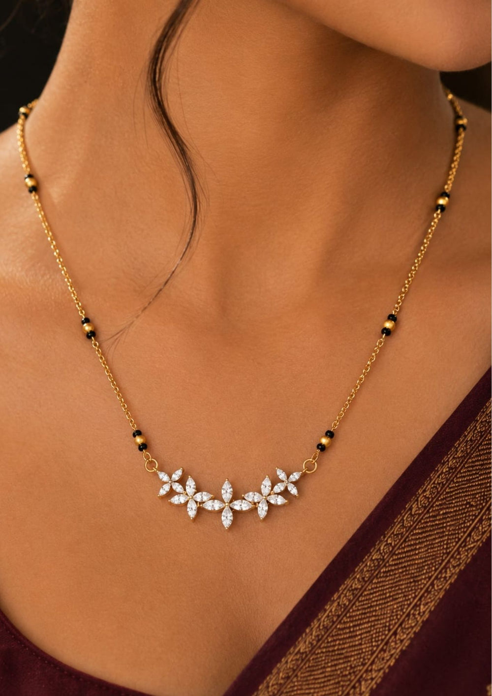 A delicate gold chain necklace with a central cluster of clear stones in a leaf or floral motif, worn on a model's neck. The necklace includes small black bead accents along the chain.