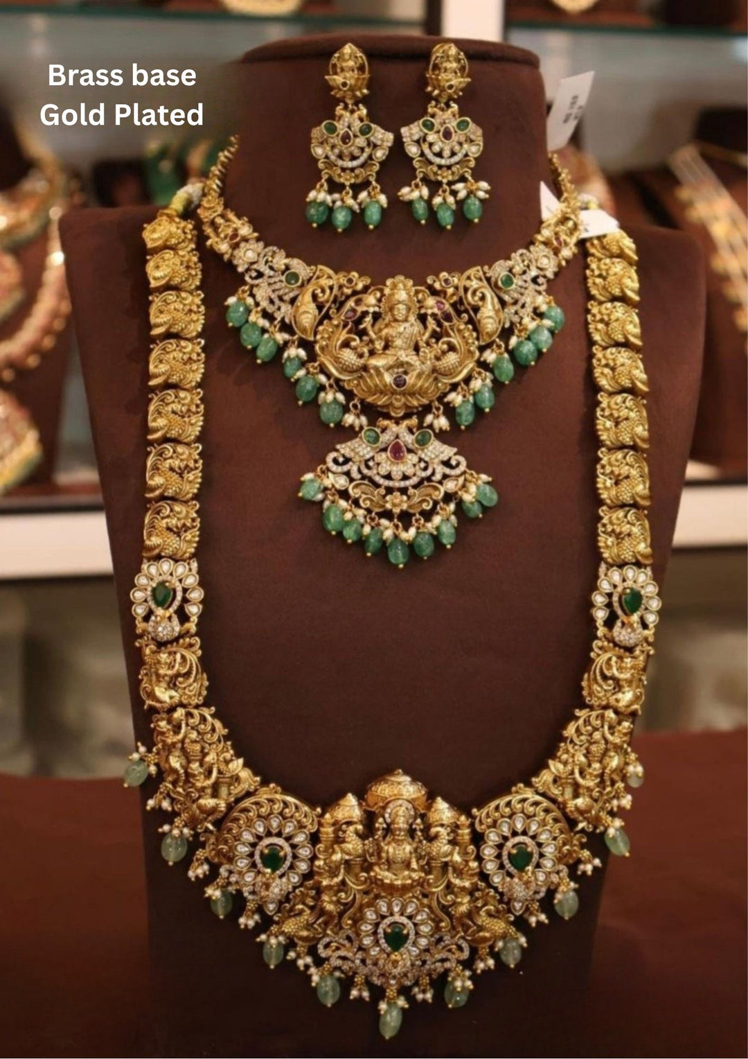 Gold-plated necklace and earrings on a mannequin bust with green gemstones.