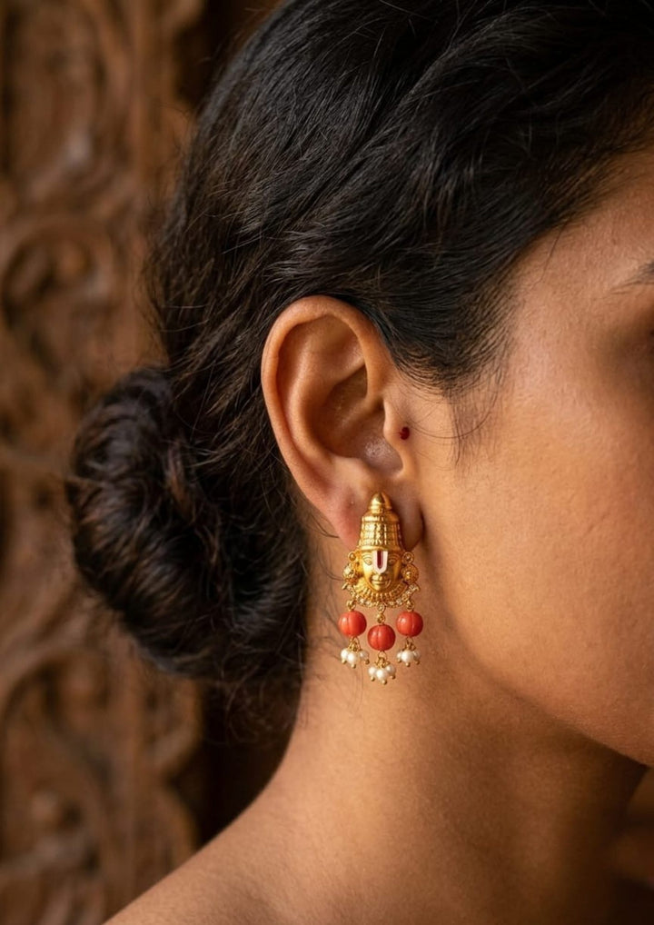 A South Indian woman wearing a Gold Plated Balaji Coral Beads earring with a polished gold finish, The design highlights a beautifully carved blalaji pendant  from a neat coral bead strand, The earrings pattern with Lord Venkateswara designs, pearl drops, guttapusalu and a smooth finish, Perfecr for festivals, poojas, and weddings