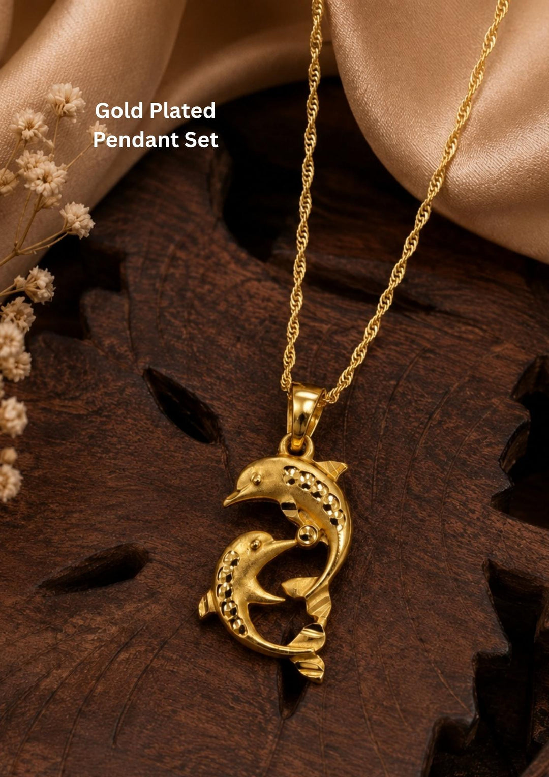 Gold-plated pendant necklace featuring a dolphin design with small clear stones, displayed on a dark wooden surface with beige satin fabric and dried flowers. Text overlay reads 'Gold Plated Pendant Set'.