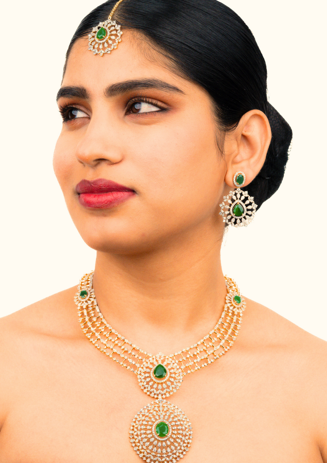 South Indian omen Wearing a Zircon diamond gold-plated necklace and earrings set designed with 3 row zircon diamonds and in the middle it is designed with green emerald stone and it also has matching earrings designed in the leaf pattern with green emerald stud on the top and it also had magtikka perfect for weddings, bridalwear, festivals and its anti fade color