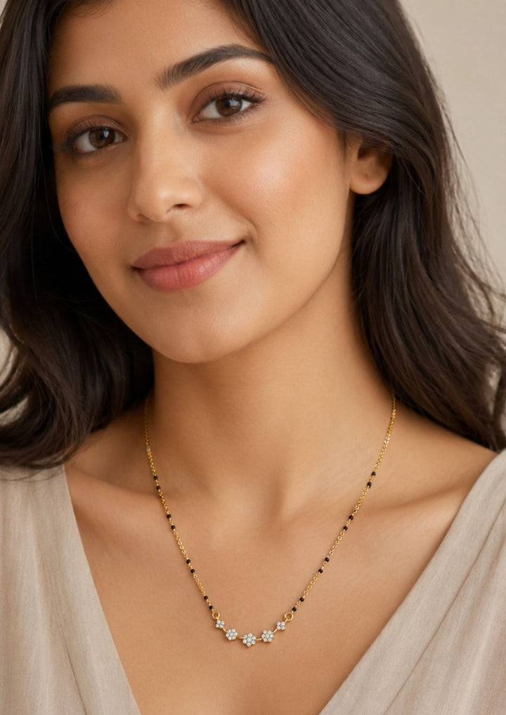 Woman wearing Gold plated black beads mangalsutra featuring delicate floral zircon motifs beautifully arranged along the centerpiece. Designed with a lightweight mangalsutra chain, perfect for everyday elegance and festive styling.