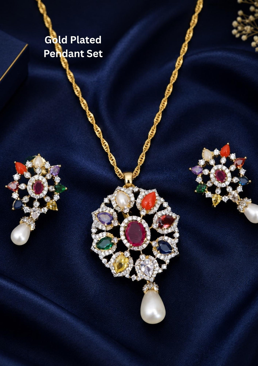 Gold-plated pendant necklace and matching earrings set displayed on dark navy blue satin fabric. The central pendant features a gold-toned floral design with multiple colorful gemstones and a dangling pearl, with matching earrings arranged symmetrically.