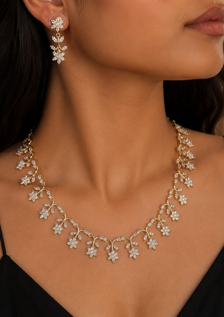Gold-plated zircon diamond necklace and matching stud earrings. The necklace features a vine design with floral and leaf motifs set with clear stones. Beautiful zircon diamond gold plated floral necklace set featuring delicate flower and leaf motifs with matching earrings. Perfect for weddings, parties, festive occasions, and elegant daily styling.