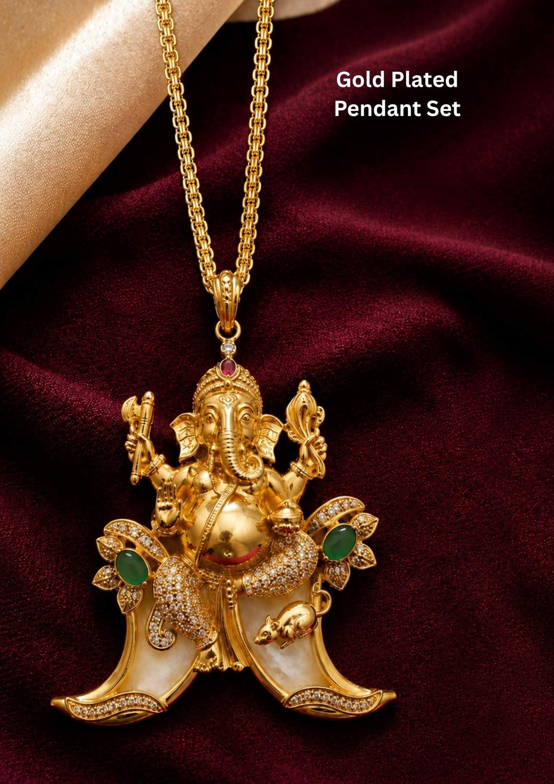 A traditional gold plated temple style pendant featuring an intricately sculpted idol of Lord Ganesha seated above a curved double tiger claw (pulinakha) motif. The piece is adorned with shimmering white crystals, ruby-red crown details, and green stone side accents, held up by a hand with blurred jewelry store displays in the background.