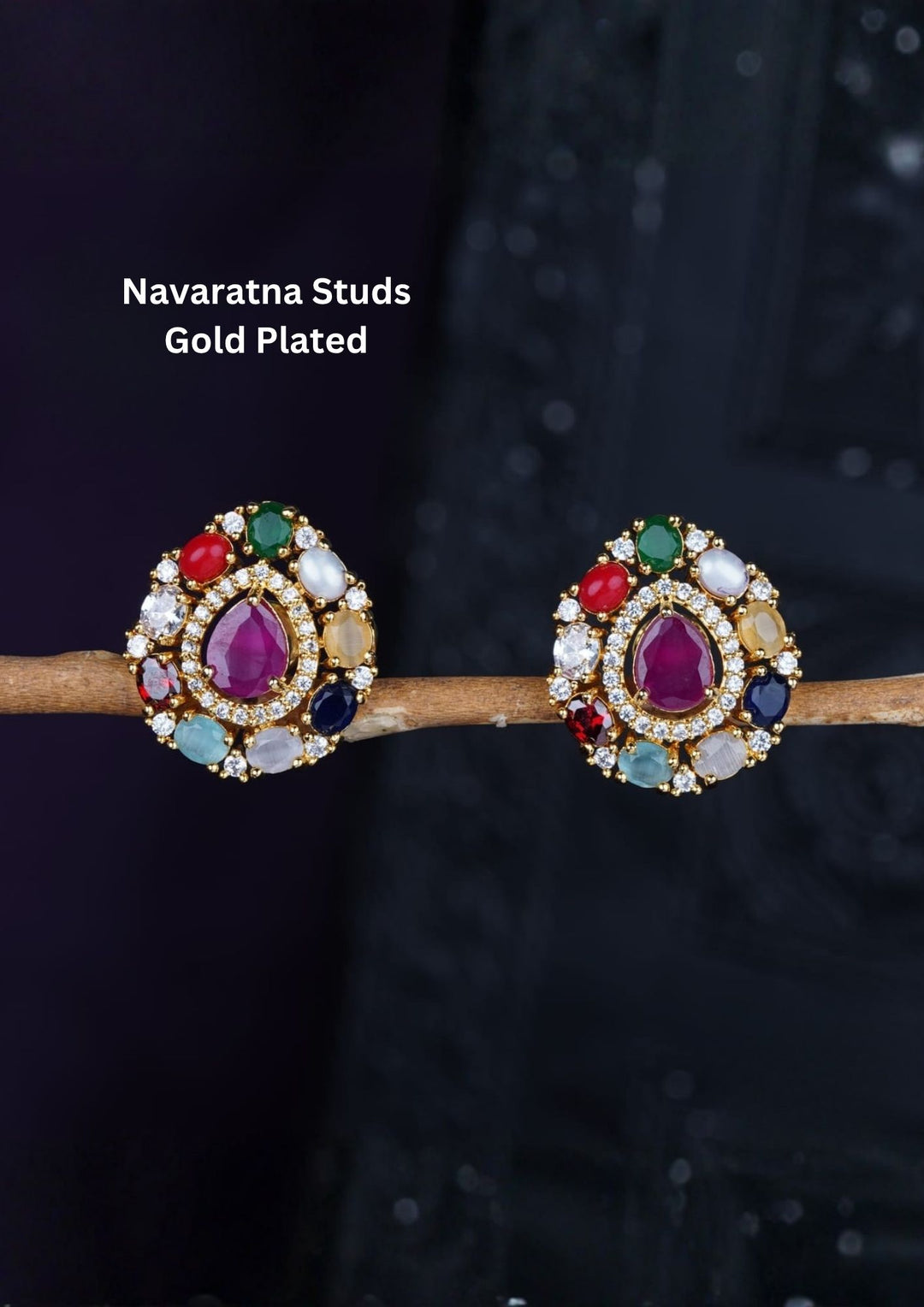 A pair of classic gold plated Oval stud earrings showcasing the traditional Navaratna design with nine distinct multi-colored gemstones. The center holds a smooth oval pink ruby stone, encircled by eight tear-drop shaped petals representing pearl, coral, emerald, sapphire, and other colorful crystals. The set is crafted with a highly polished golden finish and comfortable post backings.