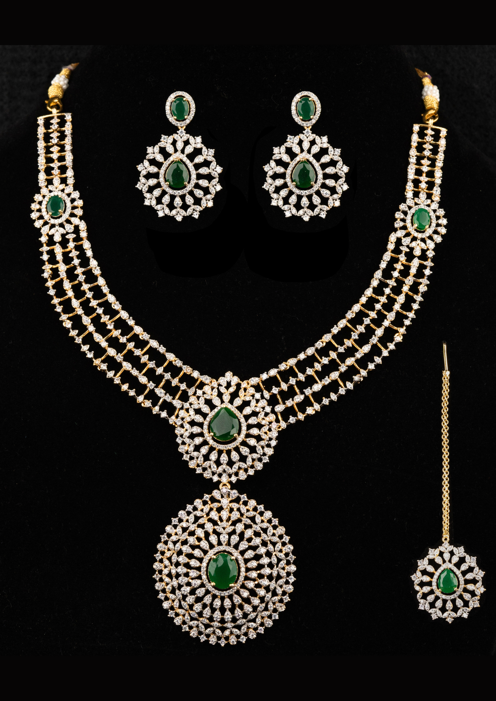 Zircon diamond gold-plated necklace and earrings set designed with 3 row zircon diamonds and in the middle it is designed with green emerald stone and it also has matching earrings designed in the leaf pattern with green emerald stud on the top and it also had magtikka perfect for weddings, bridalwear, festivals and its anti fade color