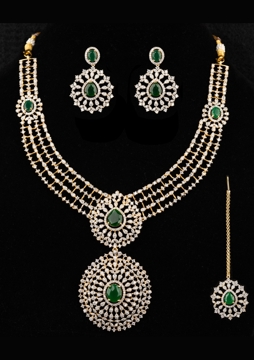 Zircon diamond gold-plated necklace and earrings set designed with 3 row zircon diamonds and in the middle it is designed with green emerald stone and it also has matching earrings designed in the leaf pattern with green emerald stud on the top and it also had magtikka perfect for weddings, bridalwear, festivals and its anti fade color