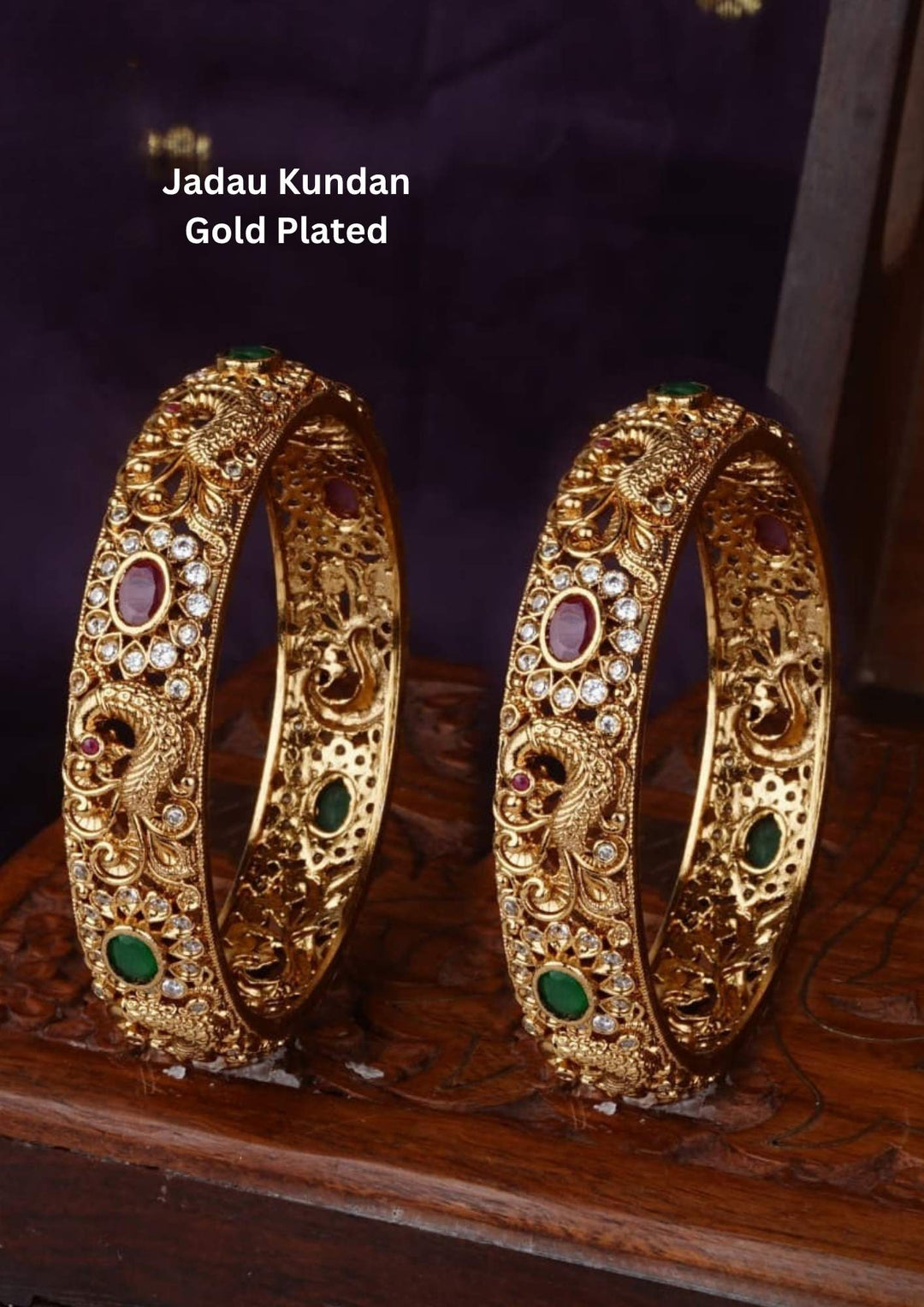 gold-plated jadau kundan peacock bangles designed with multiple rows of eclipse-cut red Kemp stones, green emrald with white crystal borders, and an ornate golden peacock design centered with a water drop green stone. It is lightweight, skin-friendly, and anti-fade bangles are perfect for poojas, festive wear, and dailywear.