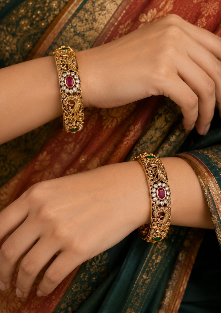 Close-up of a south indian woman's hands wearing jadau kundan Peacock Bangles design with ruby-red and green stones and a golden peacock motif with a green stone accent, offering a rich, bridal-style look perfect for weddings, festivals, bridal look and functions.