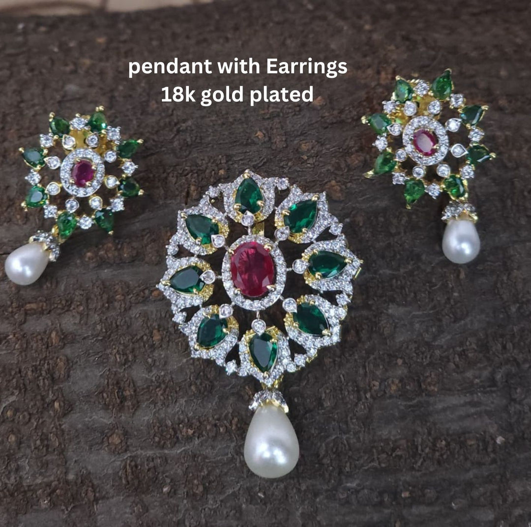 Gold-plated pendant necklace and matching stud earrings displayed on a black velvet jewelry bust. The necklace features a detailed floral pendant with red, green, and blue stones, while the matching earrings are shown above the bust.