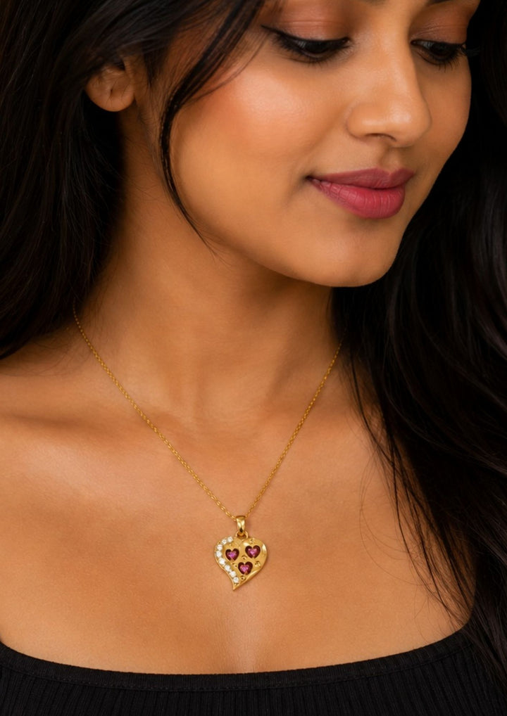 Close-up of a woman wearing The main heart features an asymmetric, sweeping border on the left side encrusted with a row of small, clear sparkling stones. Inside the main heart, there are three cut-out heart shapes, each Nesting a vibrant, pinkish-red stone (resembling rubies or pink crystals) at its center..