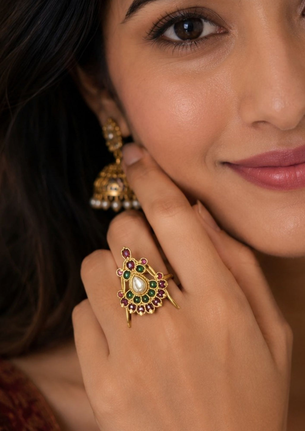 South indian women wearing Traditional gold plated adjustable finger ring featuring an intricate antique-inspired design adorned with ruby pink and emerald green kemp stones. The centerpiece showcases a pear-shaped white kundan stone surrounded by circular stone detailing in a graceful temple jewelry pattern. The adjustable open-back design ensures a comfortable fit while adding an elegant ethnic touch suitable for weddings, festivals and cultural occasions.