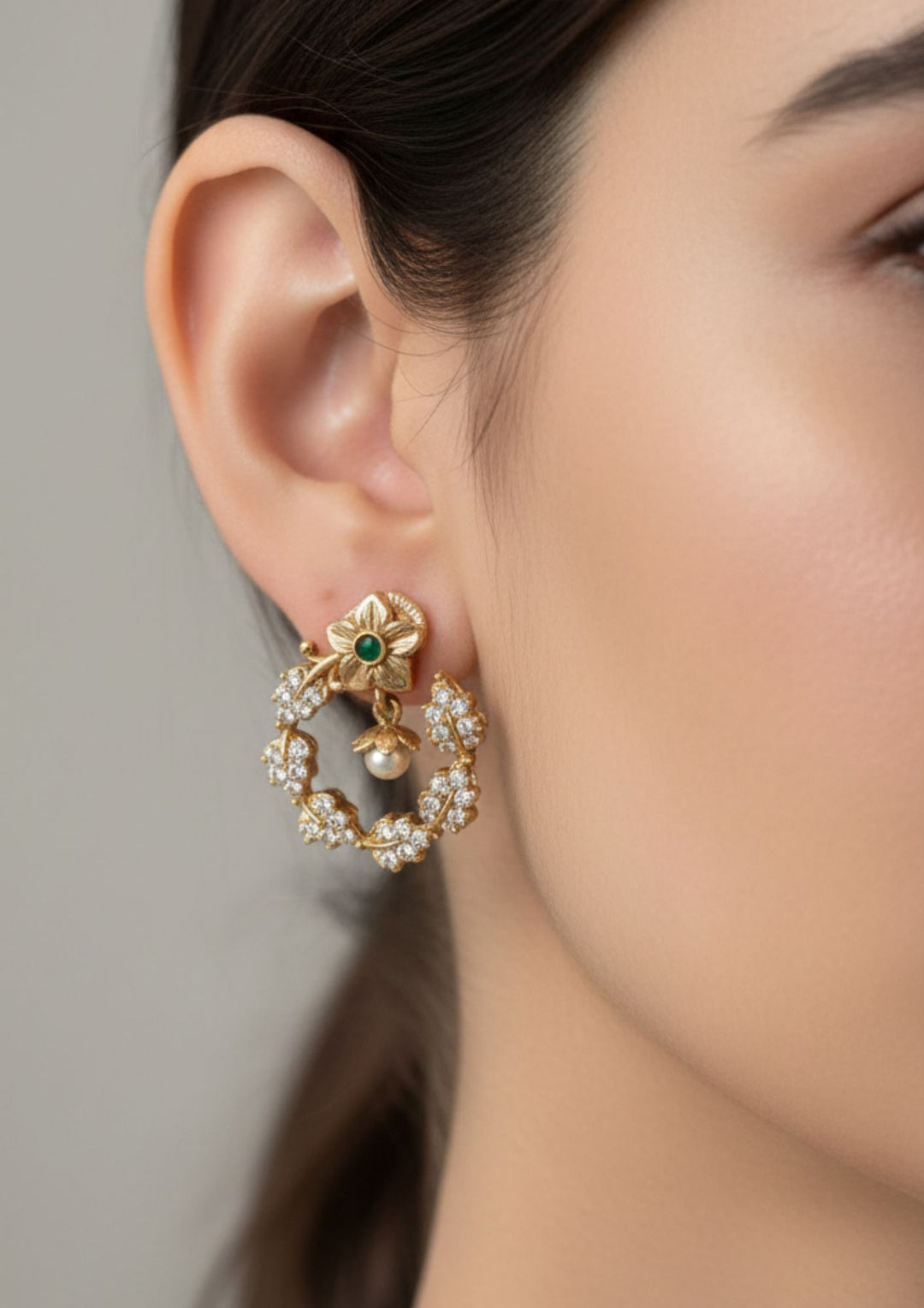  south Indian women wearing a gold plated leaf  Chandbali Earrings, The top part that sits on the earlobe is shaped like a beautifully sculpted gold flower. It has five neat petals with a tiny, round green stone fixed right in the center. Below the top flower hangs a large, open crescent ring. This ring is styled with a delicate leaf-and-vine pattern. The entire ring is encrusted with tiny, sparkling white zircon stones set in clusters that look like shimmering diamond leaves. perfect for dailywear