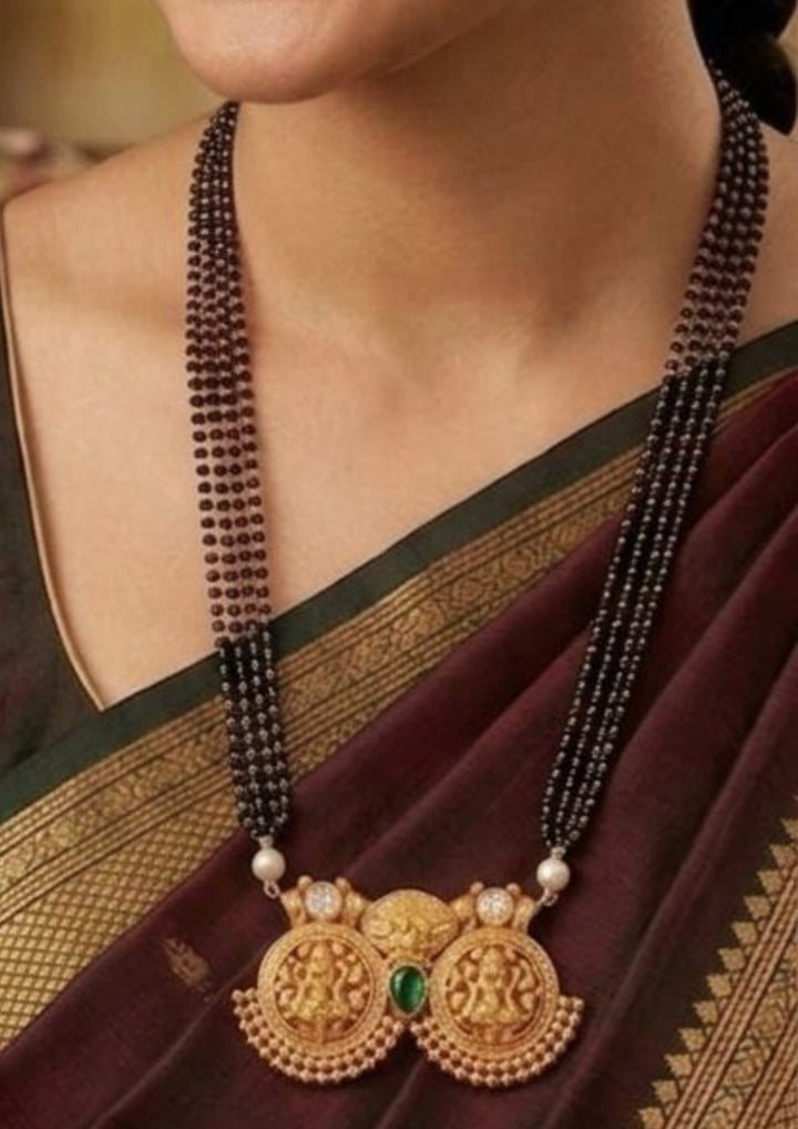 soth indain women wearing a Traditional necklace with a gold laxmi devi pendant and green gemstone with very clear look indain women's can ware for weeding's ,  festivals and daily wear