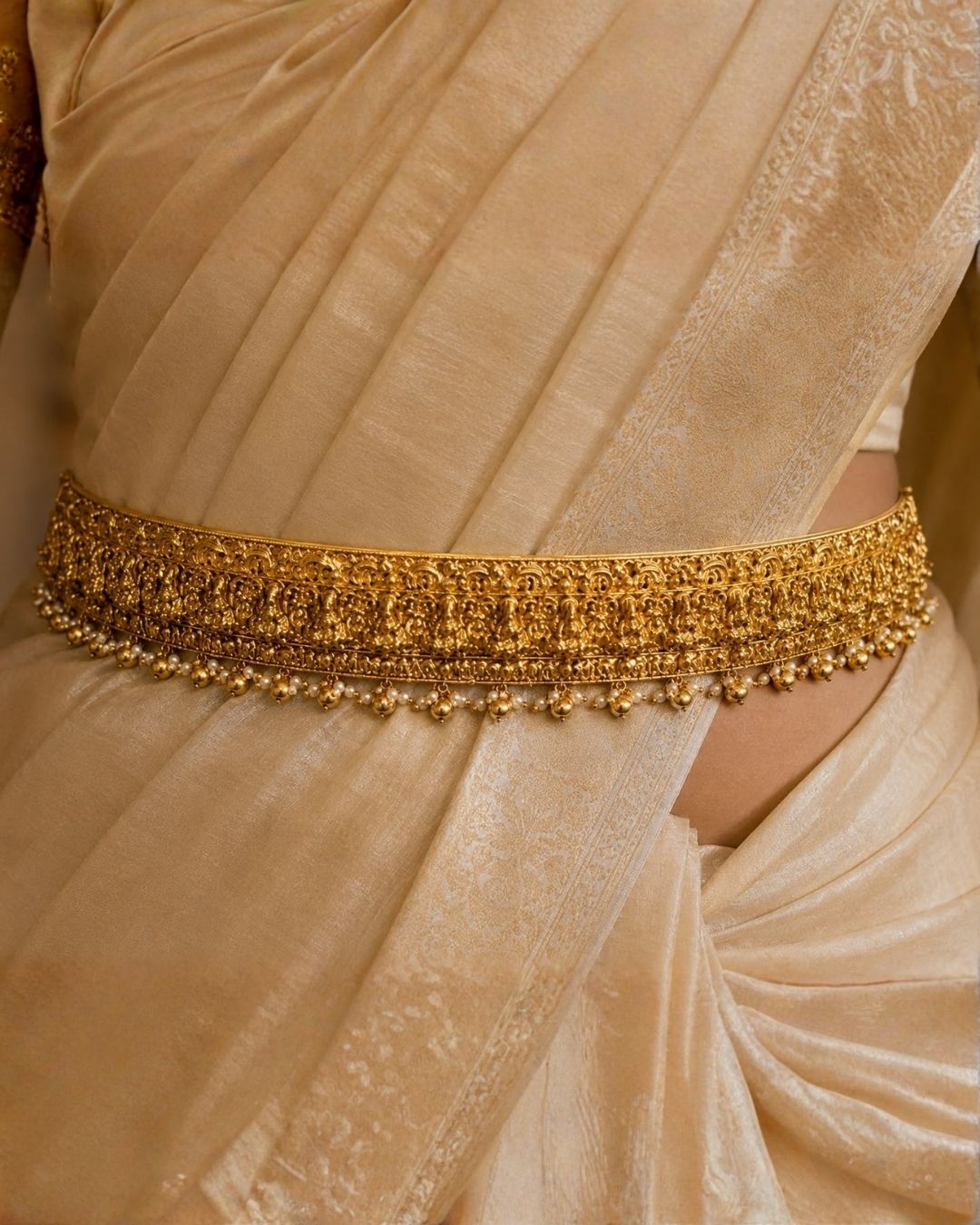 Beautiful traditional gold plated hip belt featuring intricate temple-inspired craftsmanship and dangling gold and pearl accents. Perfect for sarees, weddings, festive occasions, classical dance performances, and traditional events.