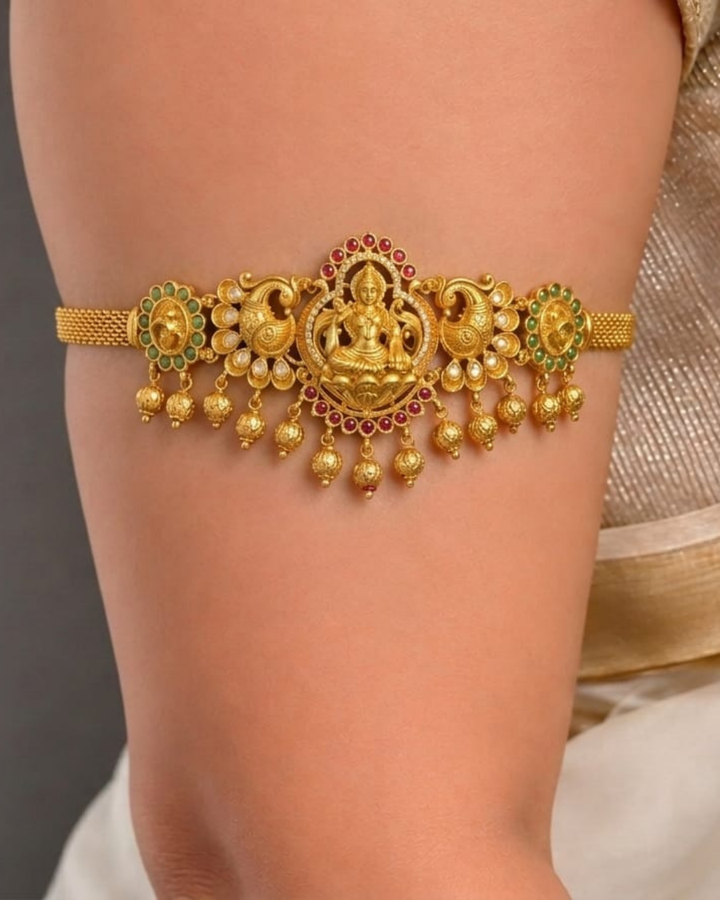 Beautiful traditional 2 in 1 gold plated choker and bajuband set featuring a detailed Goddess Lakshmi centerpiece, ornate peacock motifs, sparkling white stones, red and green accents and elegant gold bead drops.