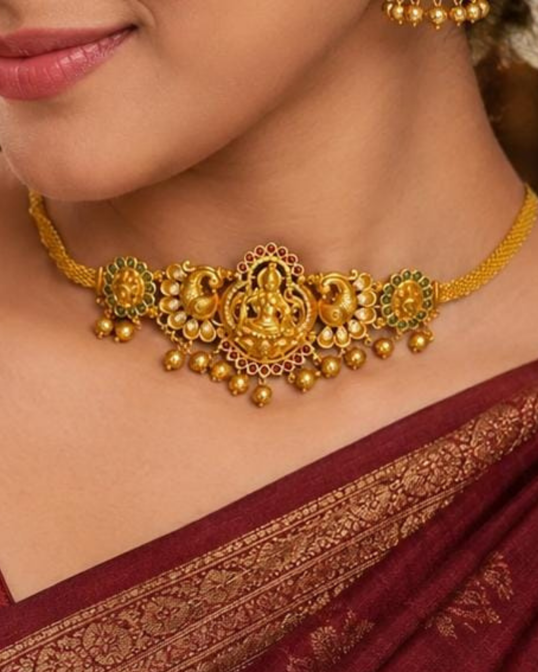 Beautiful traditional 2 in 1 gold plated choker and bajuband set featuring a detailed Goddess Lakshmi centerpiece, ornate peacock motifs, sparkling white stones, red and green accents and elegant gold bead drops.