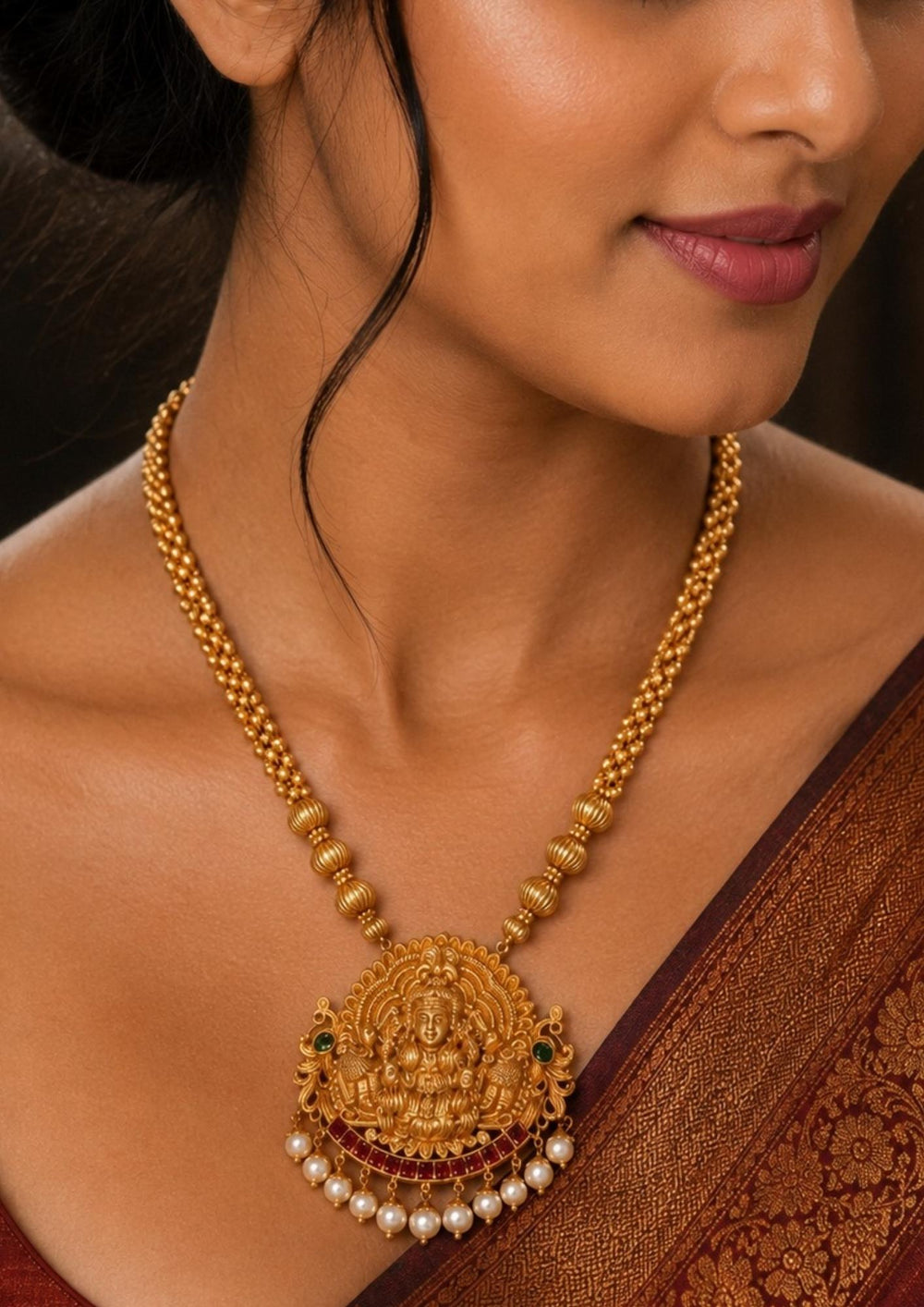 Woman wearing a Traditional jadau kundan gold plated haram necklace featuring an intricately crafted Lakshmi Devi pendant with antique detailing, ruby-tone accents and elegant pearl drops. The long beaded chain enhances the temple jewelry look, making it ideal for bridal and festive styling.